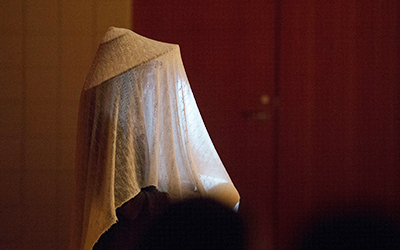 A performer with a lacy white blanket draped over their head and body