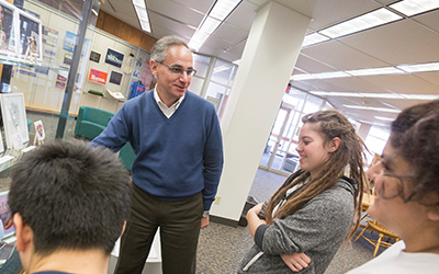 Professor Ricardo De Mambro Santos speaks to three students about an exhibit in Hatfield library