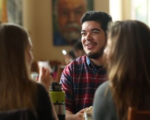 Jose Fausto sits at a table speaking to other students