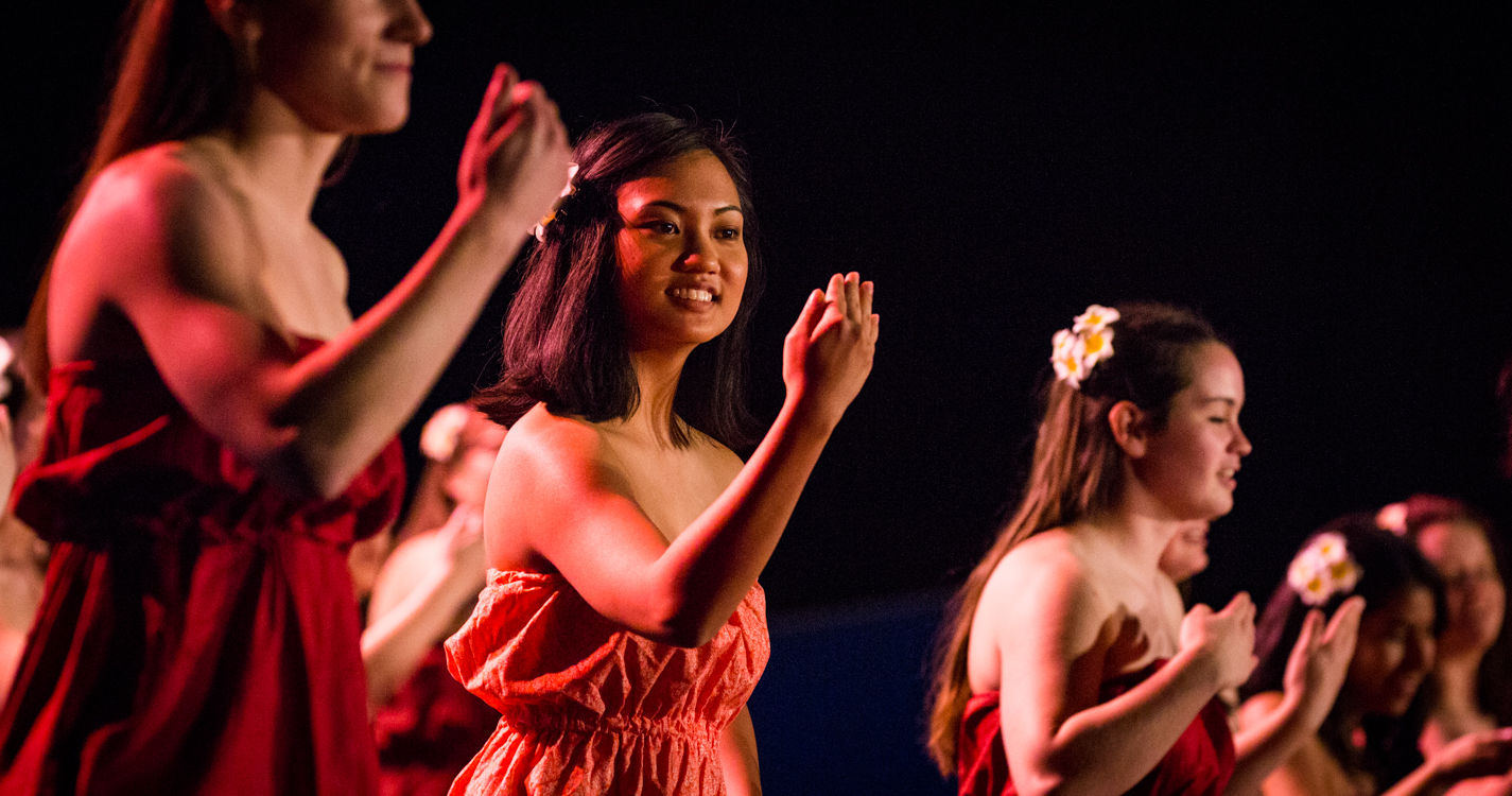 a line of women with flowers in their hair dance at the luau