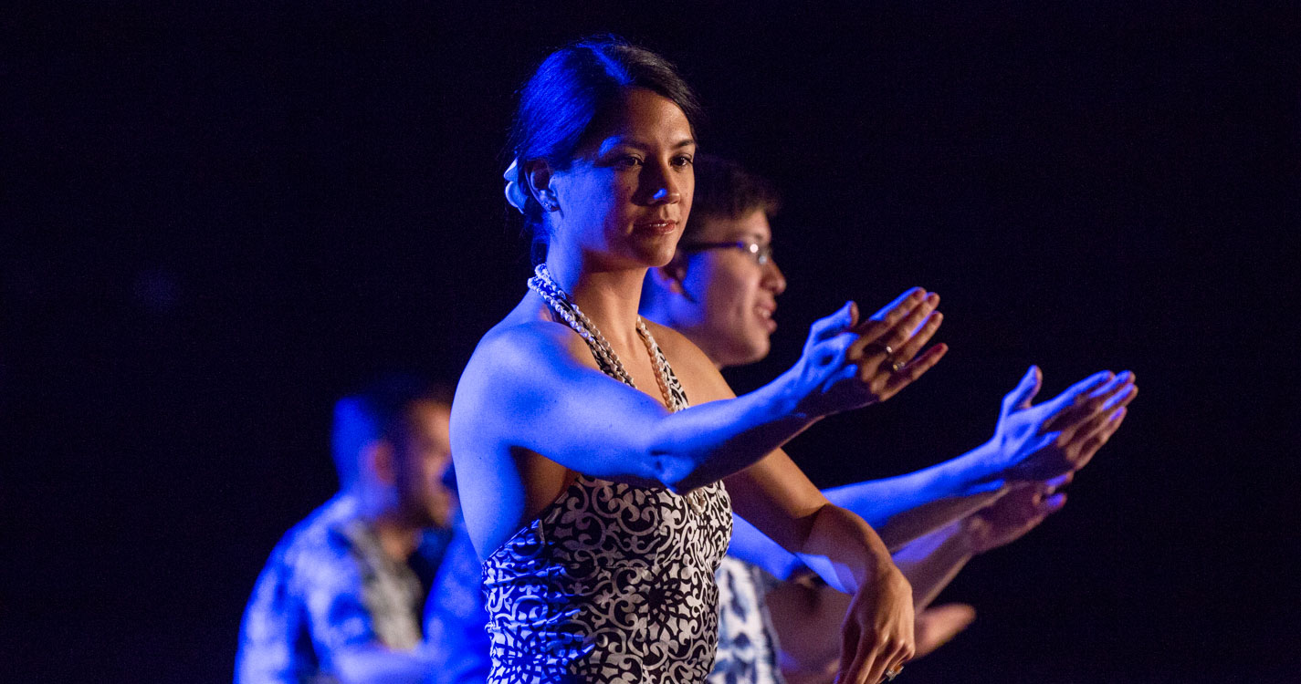 a line of women each with one arm extended dances at the luau