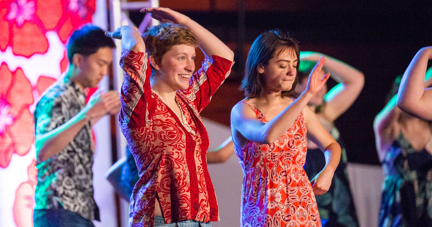 people dance onstage, smiling at the luau