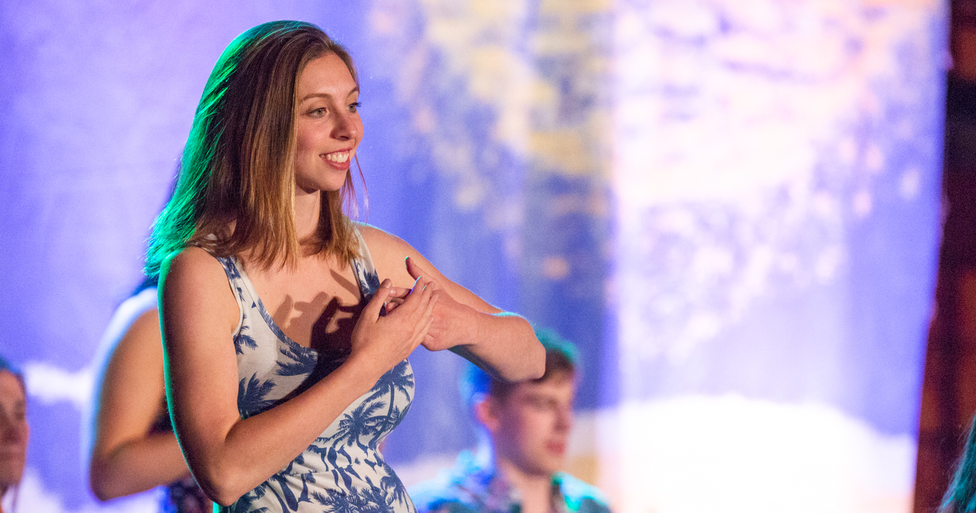 a woman makes an intricate gesture with her arms and hands while dancing in the luau