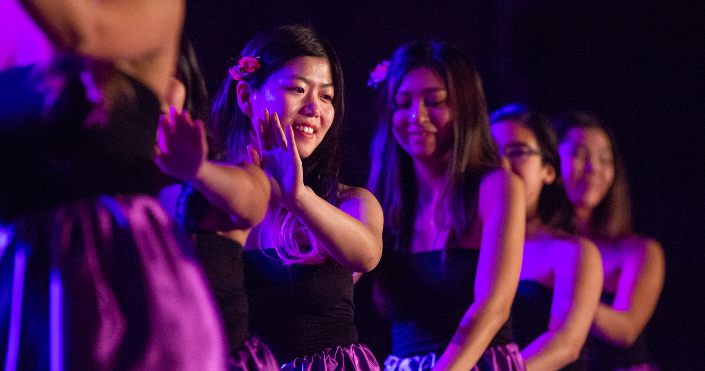 Women dance in a line in blue light at the luau