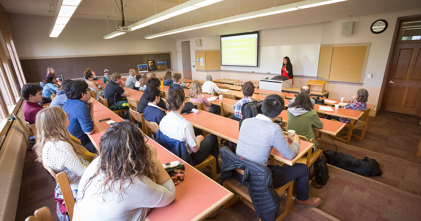 A student stands at the front of a classroom speaking to people seated at desks