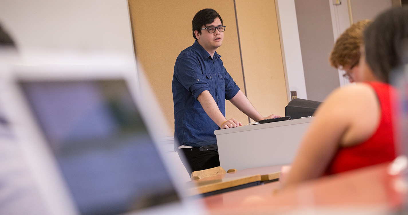 A student stands before a computer presenting at Student Scholarship Recognition Day. 