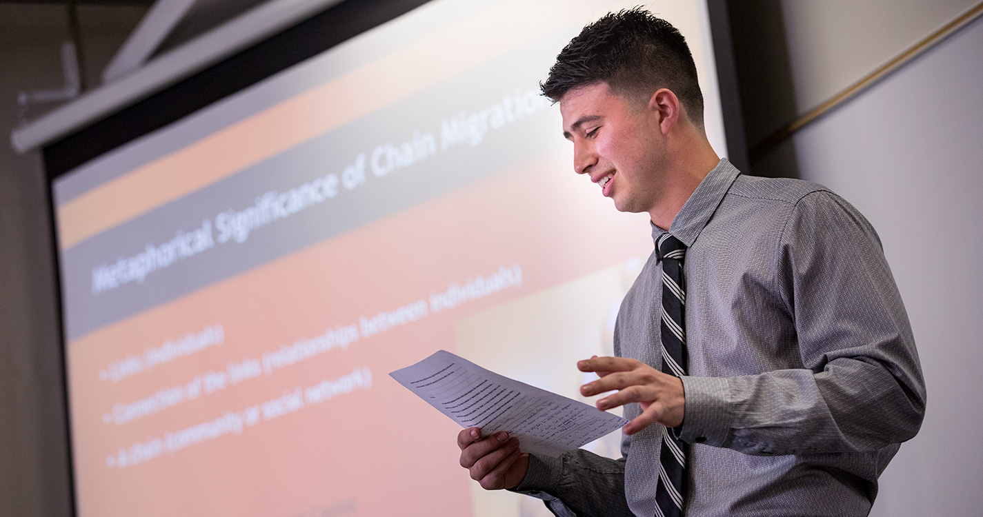 A student standing before a screen presents research at Student Scholarship Recognition Day. 