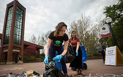 A student wearing rubber gloves sorts trash on a tarp in Jackson Plaza.