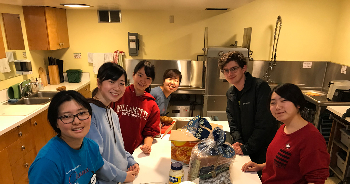 Students stand around a counter preparing a meal.