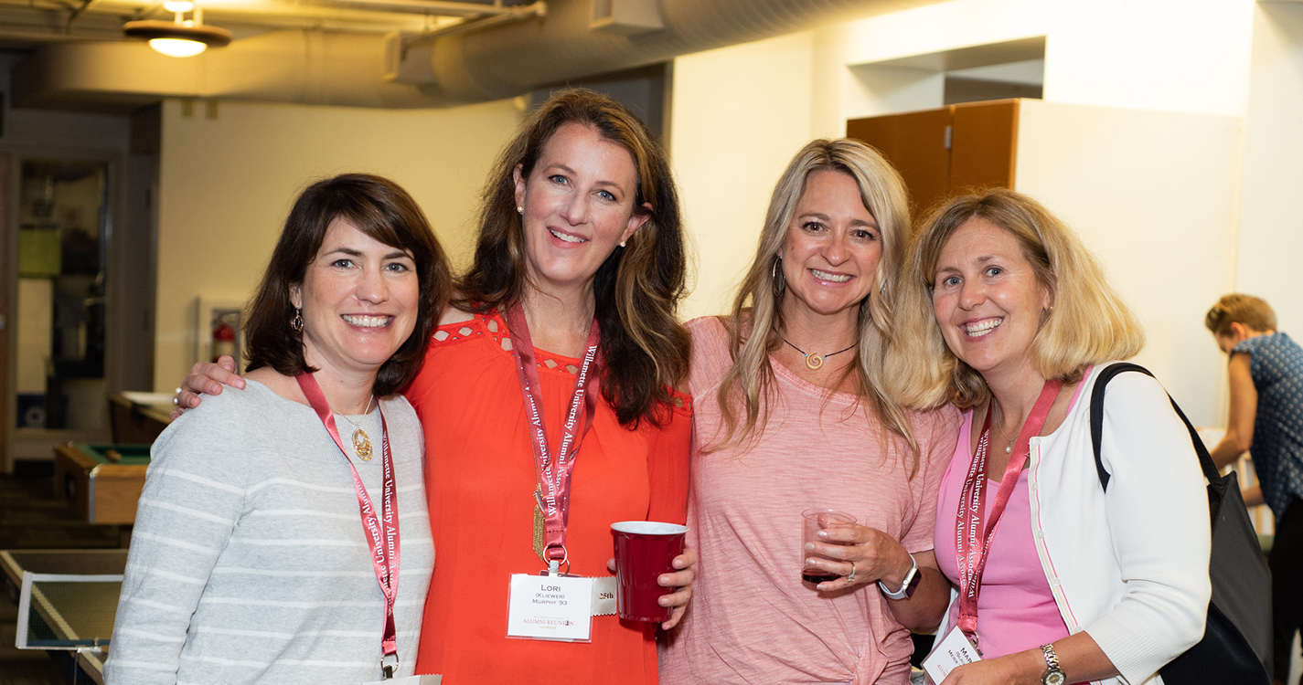 Four alumni smile with arms around one another