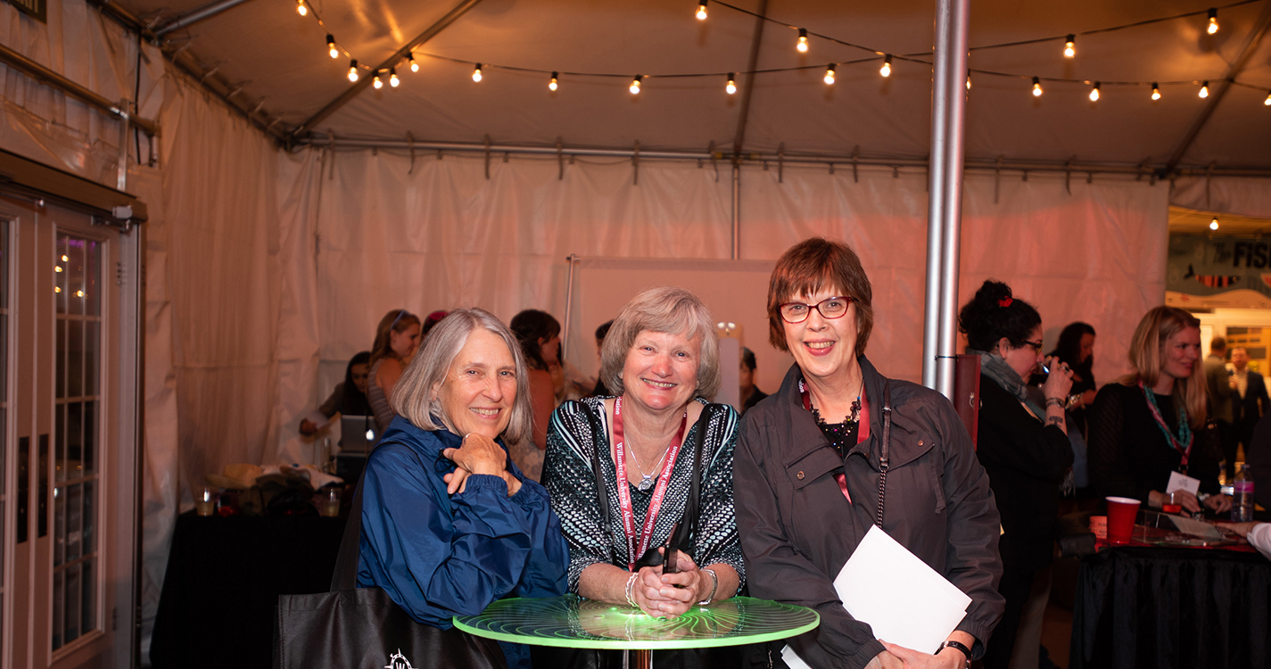 Three alumni stand at a table smiling