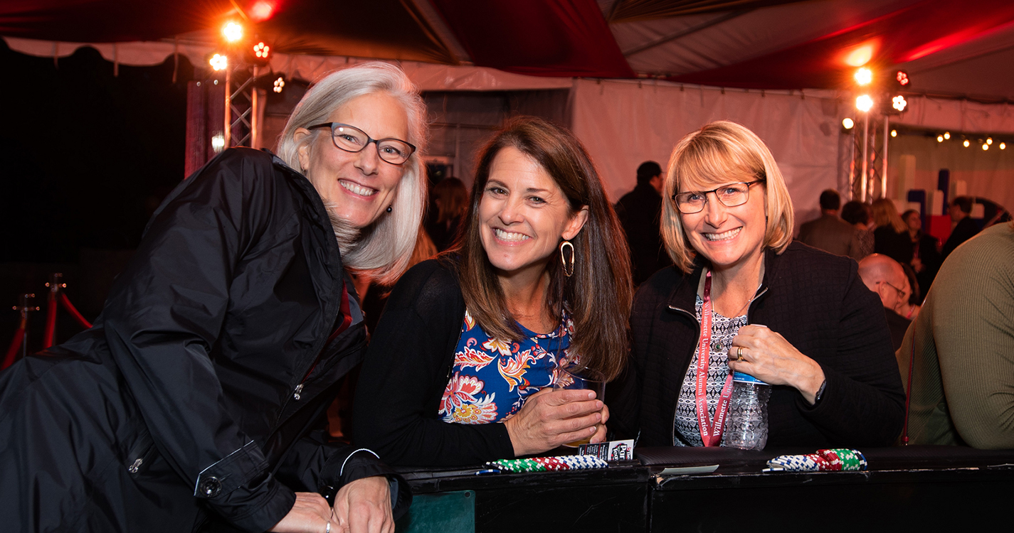 Three alumni smile at a casino table with poker chips