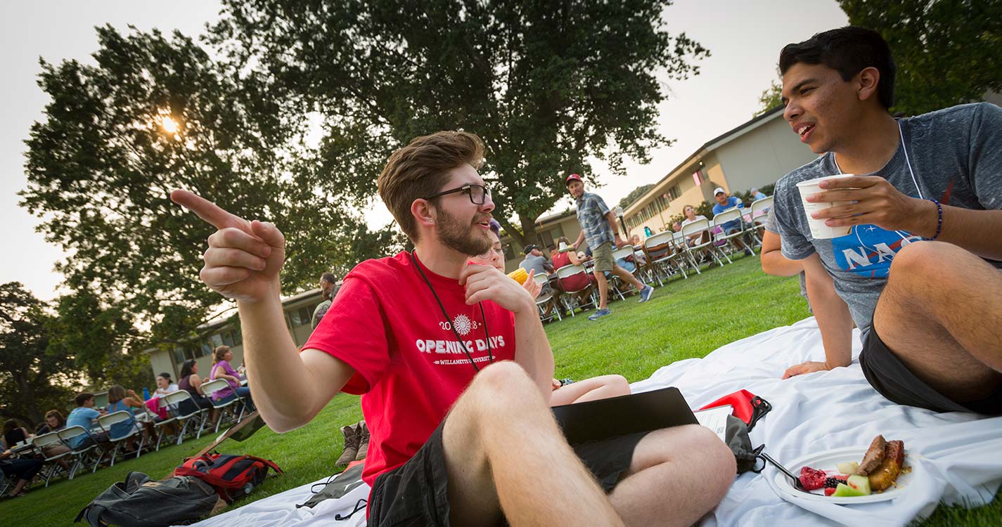 Two students sitting on a blanket have a conversation during the Opening Days Picnic Dinner.