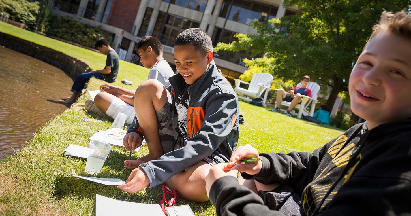 Students sitting on the bank of the Mill Stream write in notebooks