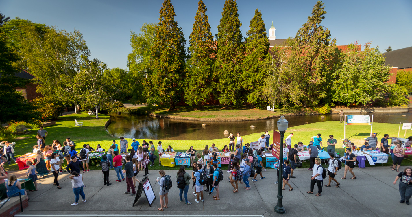 Students walk along the Mill Stream. Sidewalk lined with tables decorated with posters.