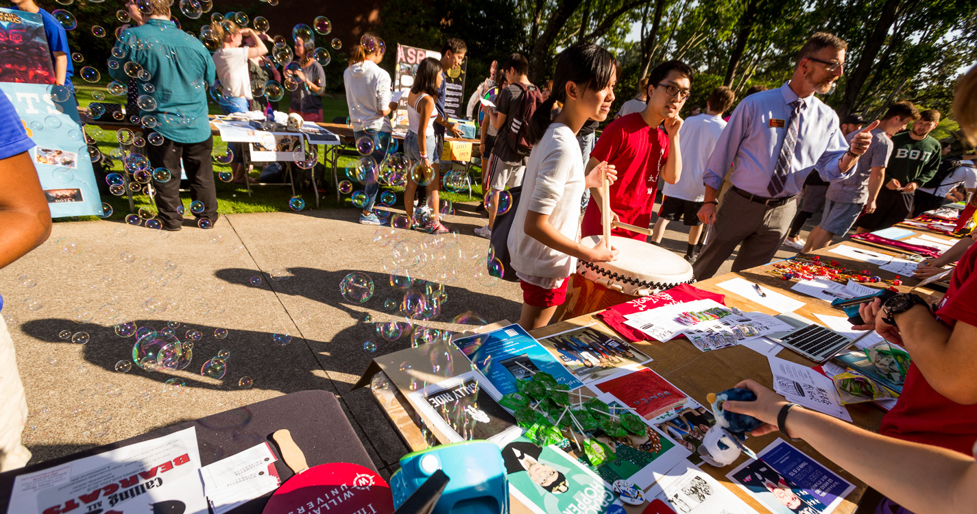 Students with a drum speak to someone at a table with bubbles blowing from a machine