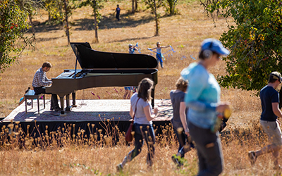 Hunter Noack plays a grand piano in the middle of a field at Willamette's Zena campus