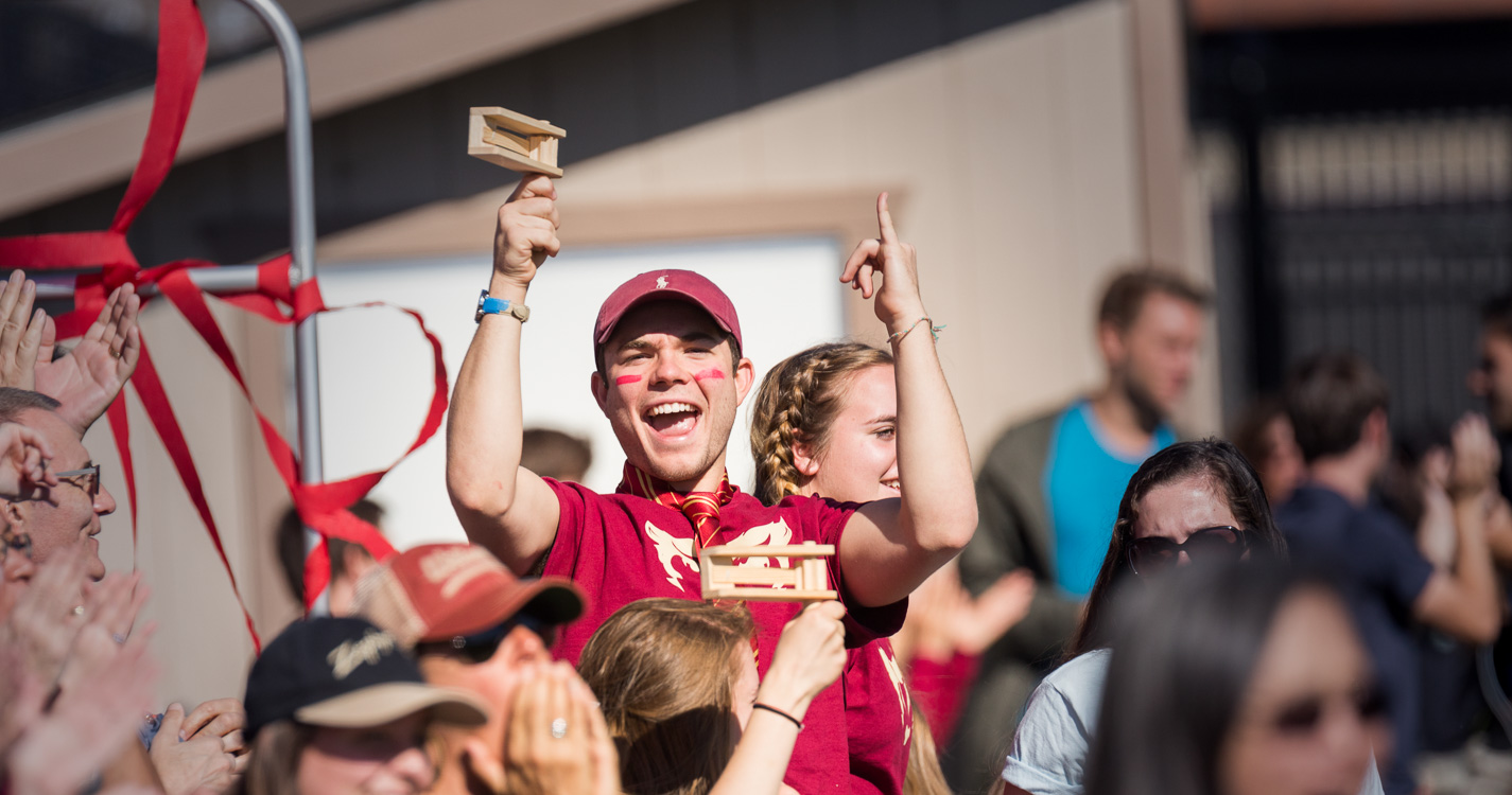 A fan in Bearcat attire smiles at cheers among the crowd at a soccer game