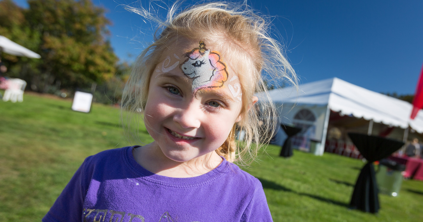 A child smiles with a unicorn painted in makeup on her forehead