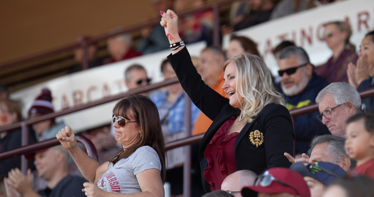 A Bearcat fan stands cheering with arm outstretched among a bunch of sitting fans