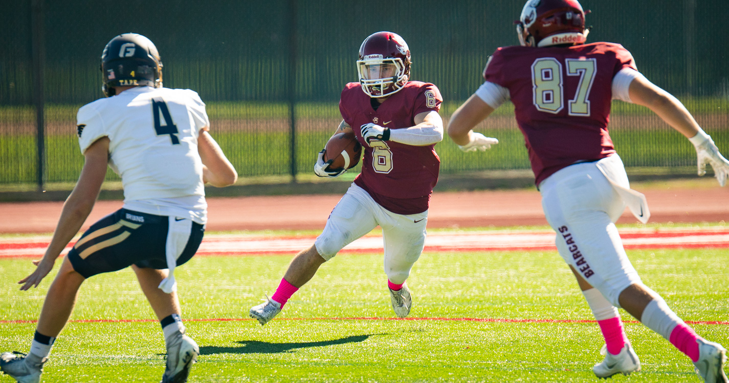 Bearcat football player cuts to his right while holding the ball to dodge a defensive player