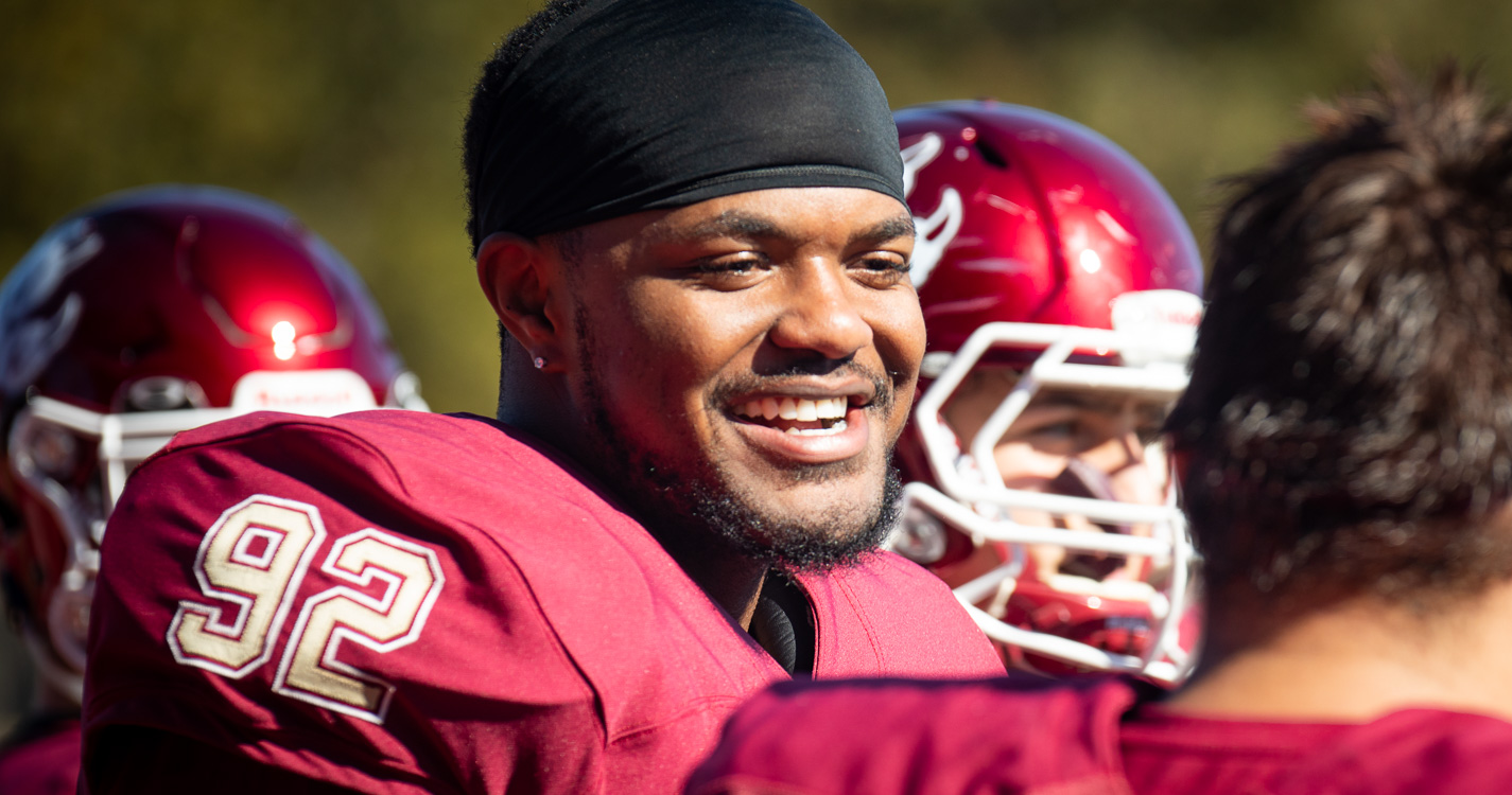 A football play with helmet removed, smiles on the sidelines