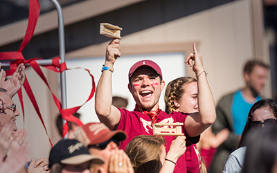 A fan in Bearcat attire smiles at cheers among the crowd at a soccer game