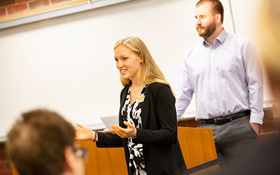 Two students stand before a classroom making a presentation