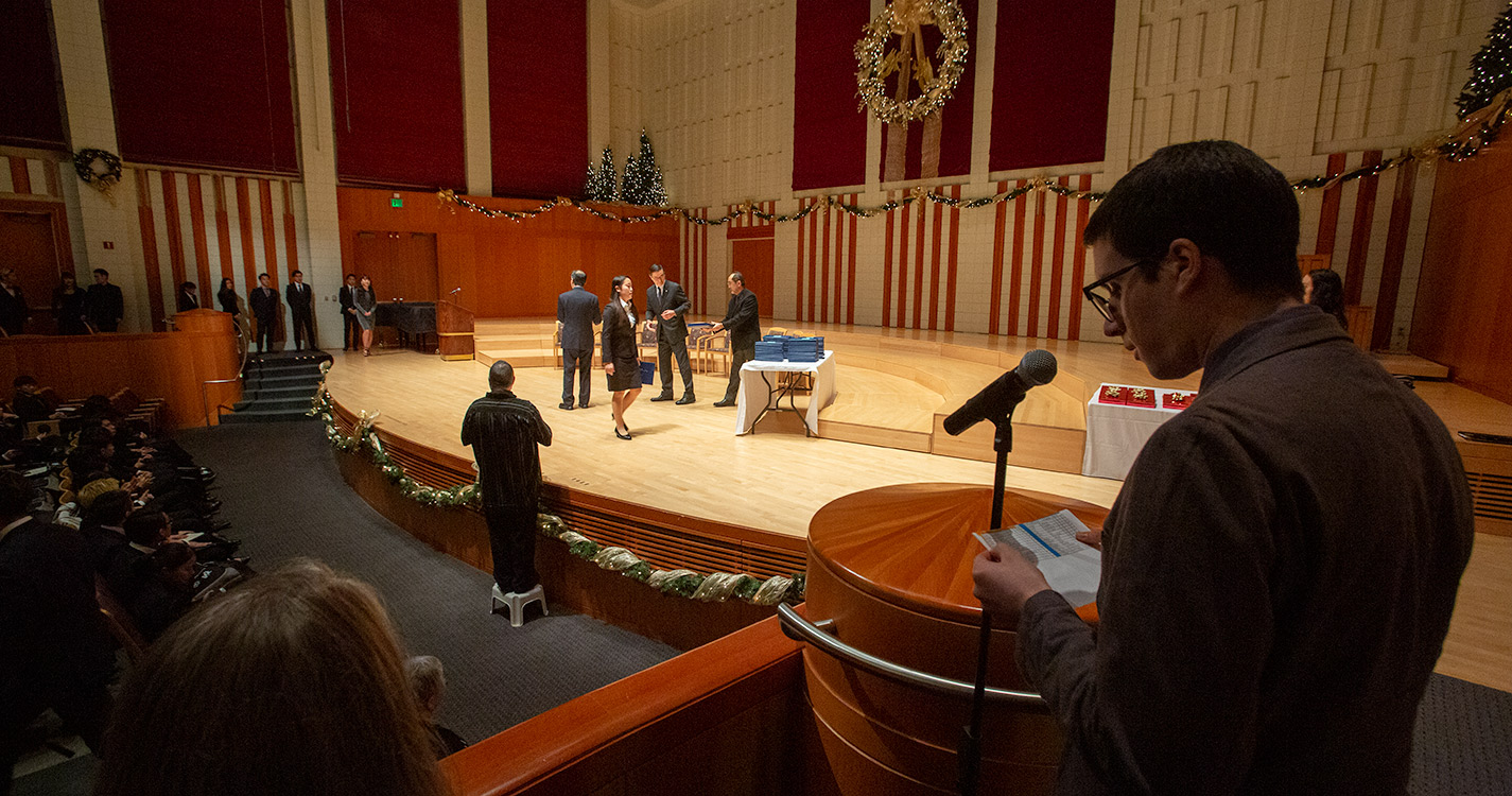 Student reads from a mic stage right, while a student receives a certificate center stage