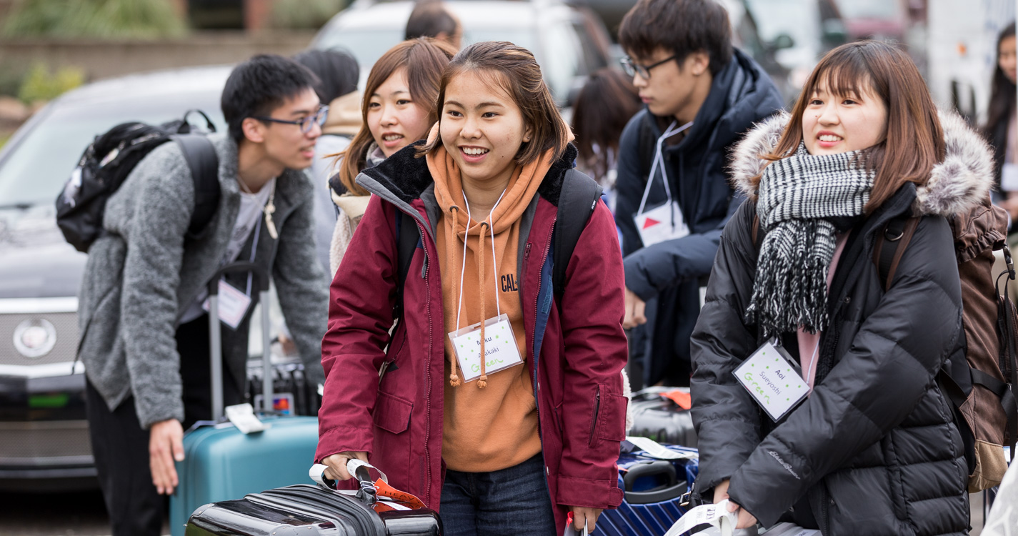 ASP students smile as they walk with luggage from a bus