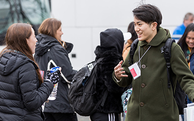 Willamette student greets an TIU student in front of a bus