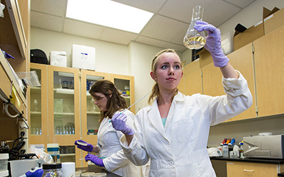 Student holds up a beaker with liquid in it to the light in a lab