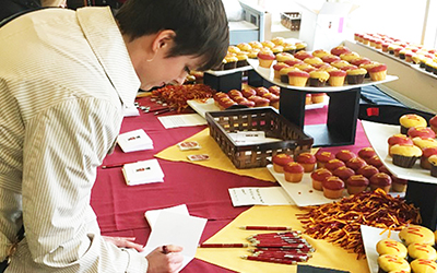 student writes a thank you note at a table with many cupcakes