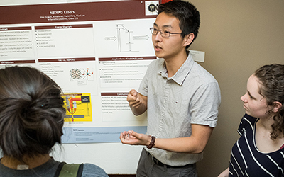 student explains poster to two gathered students