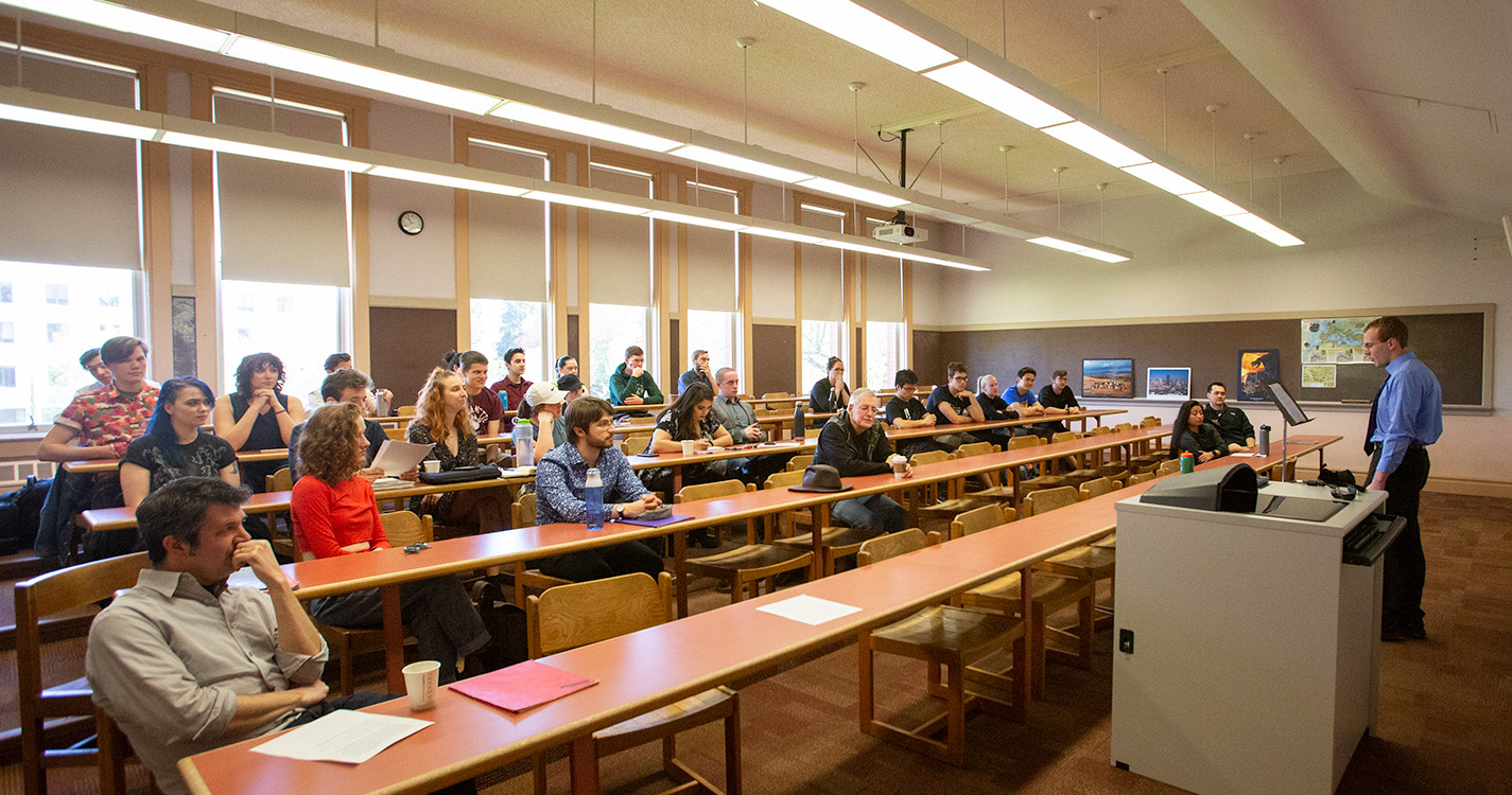 Classroom full of people listens to a student at a podium