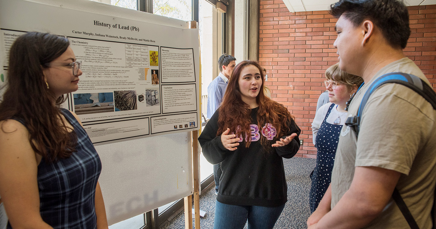 Student speaks about poster to small group gathered around