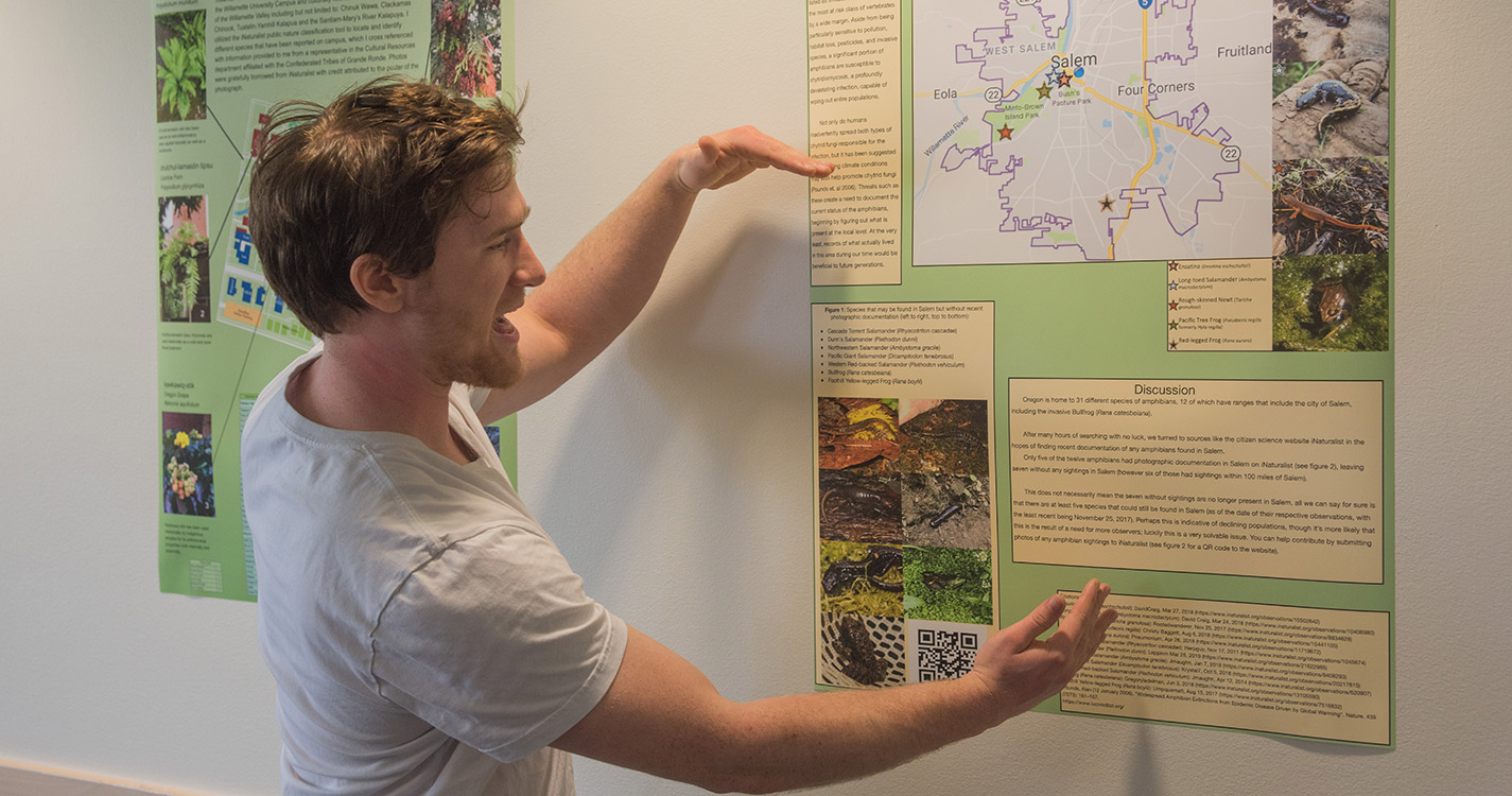 Student facing a poster extends arms in a C while making a point