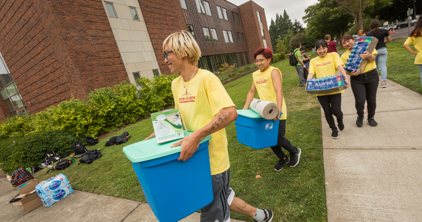 Four students in yellow shirts carry blue crates