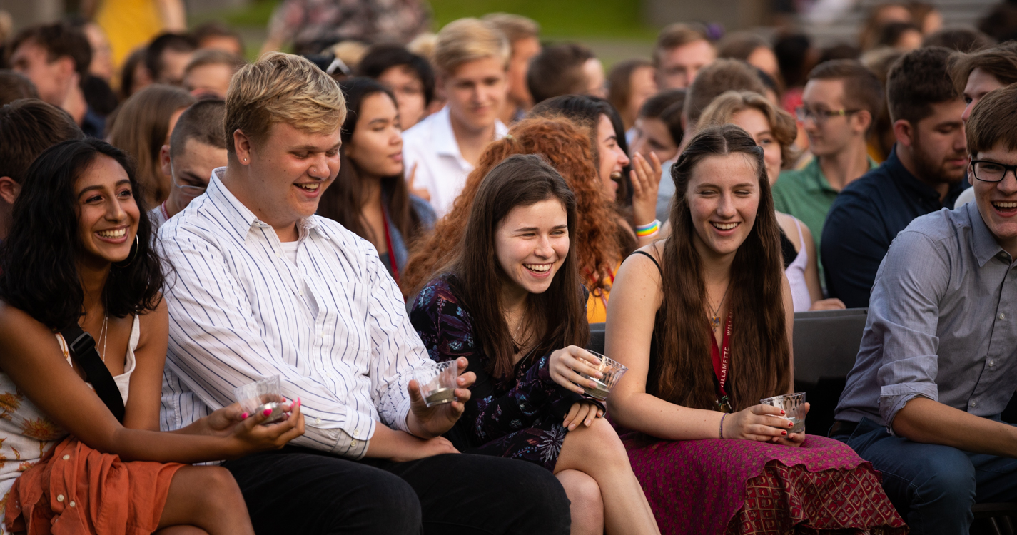 Four students seated on the Quad smile and laugh 