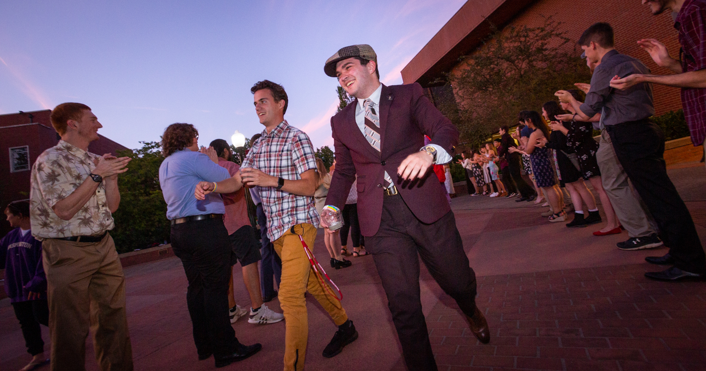 Two students smile as they pass between two lines of applauding students in Jackson Plaza