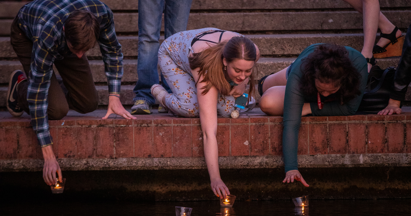 Three students lower candles onto the surface of the Mill Stream