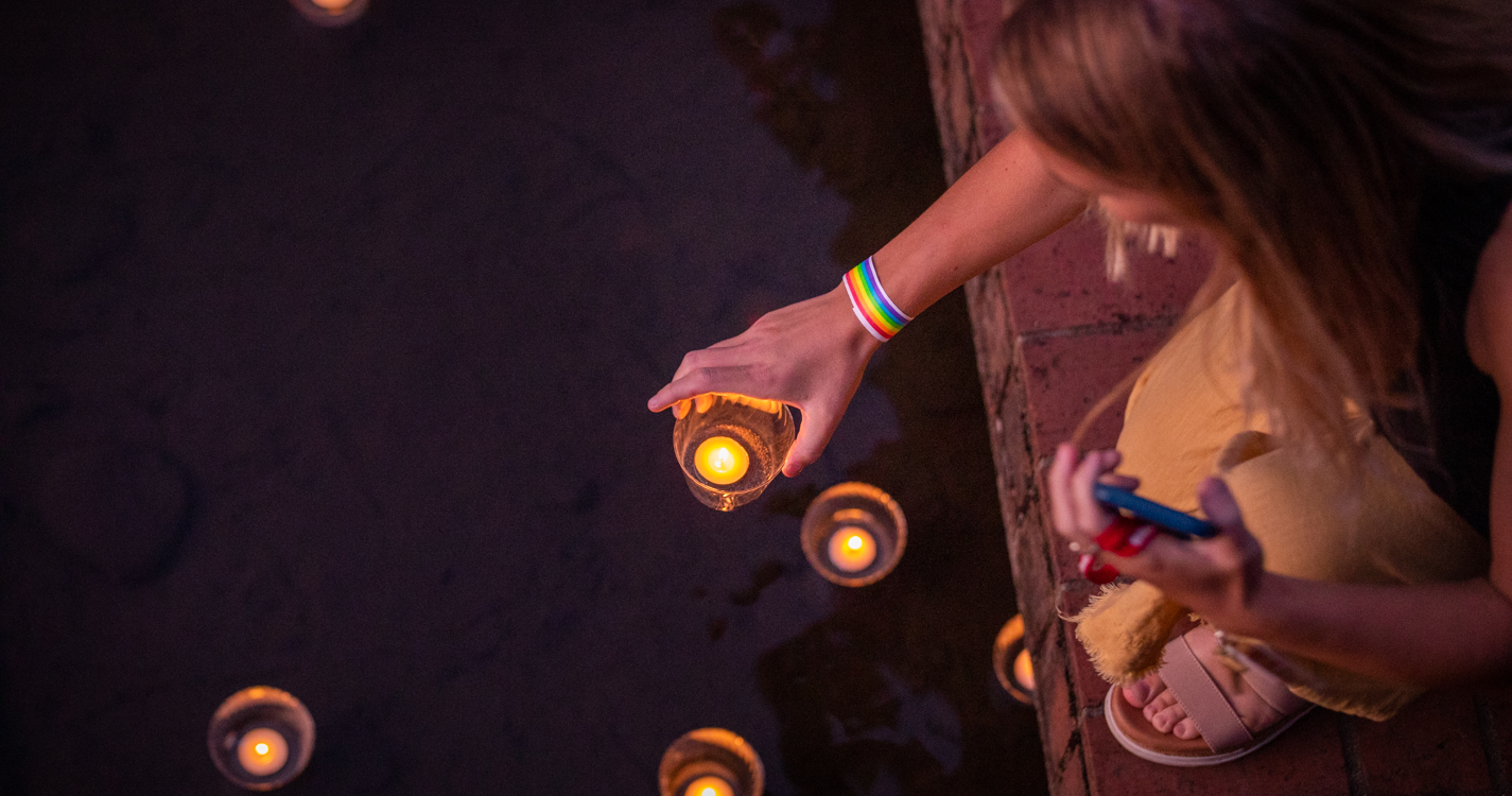 Student lowers a votive onto the surface of the Mill Stream which is peppered with votives