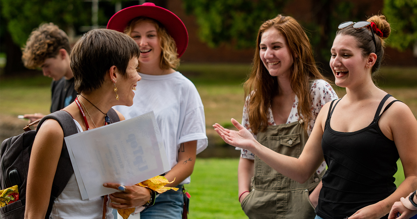 Four smiling students discuss a student organization around a banquet table outside