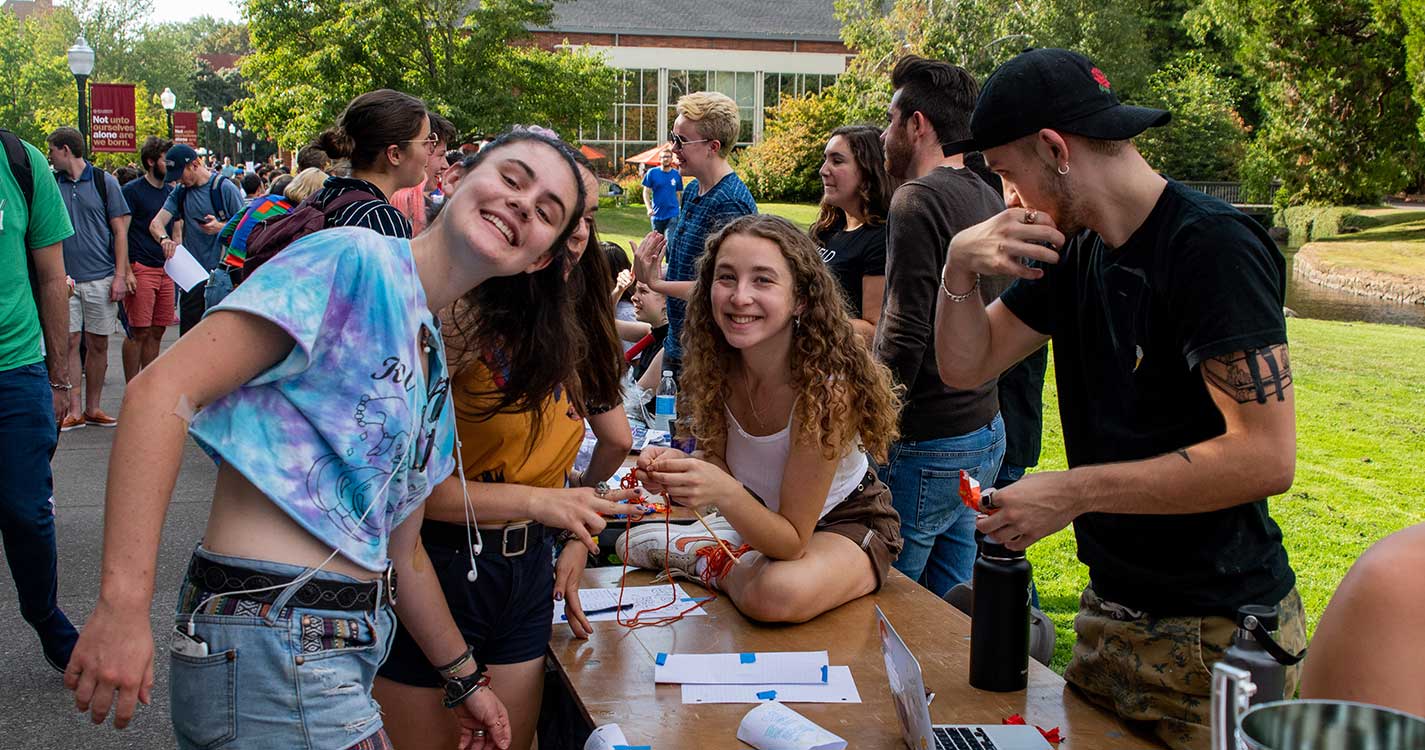 A small group of students huddles together over an activities fair table to smile for the camera