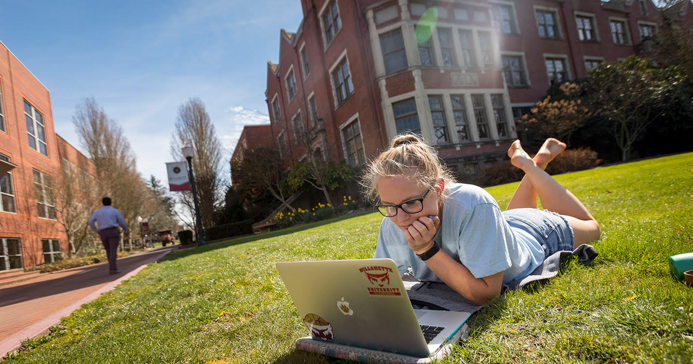 Student sitting on lawn working on laptop