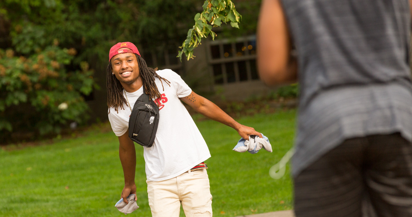 A student tosses a small bean bag outside on a field 