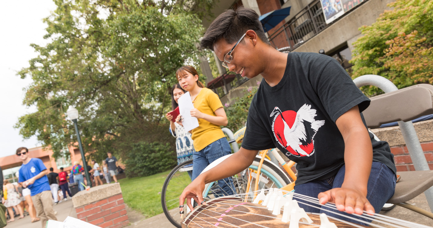 A student wearing finger picks strums a table harp-like instrument