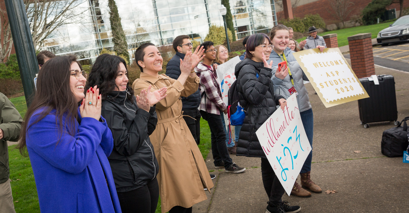 A crowd of Bearcats in winter coats, and some holding welcome signs, clap and smile 