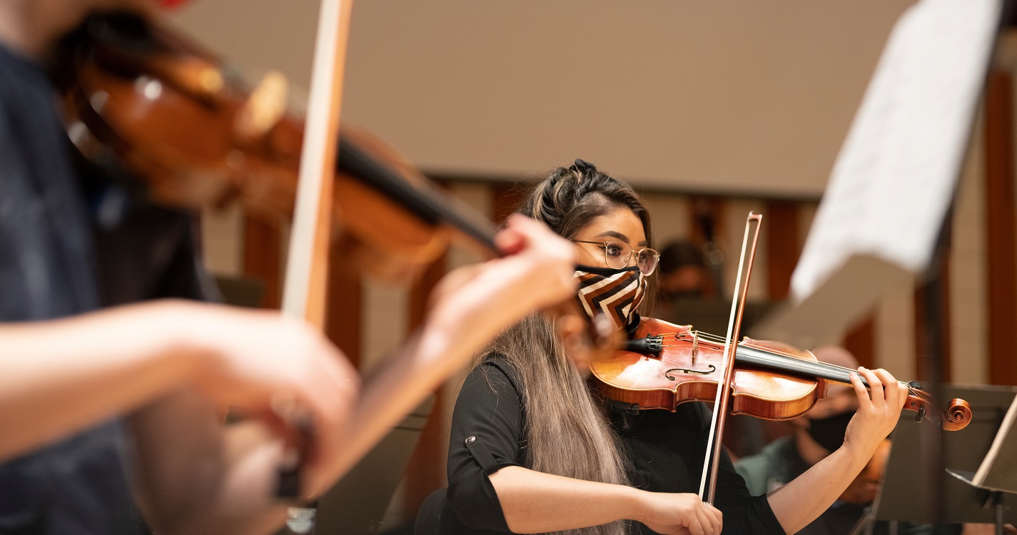 Student playing violin with facemask on in music class