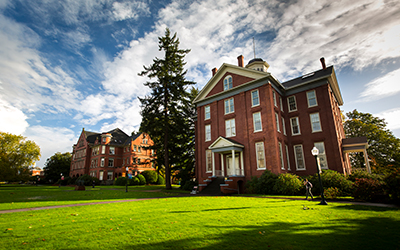 Waller Hall with green grass before it and a blue sky streaked with white clouds overhead